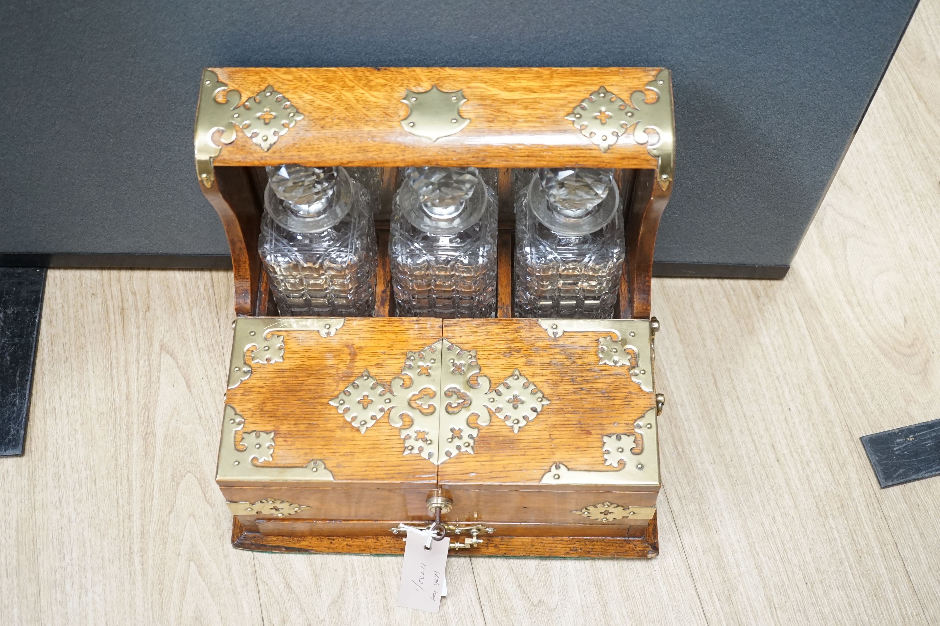 A Victorian oak and brass mounted three bottle tantalus, with base drawer and key, 36.5 cm wide